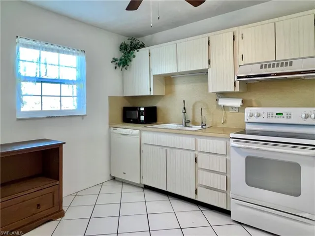 Kitchen with white appliances, light countertops, ventilation hood, light tile patterned floors, and a ceiling fan