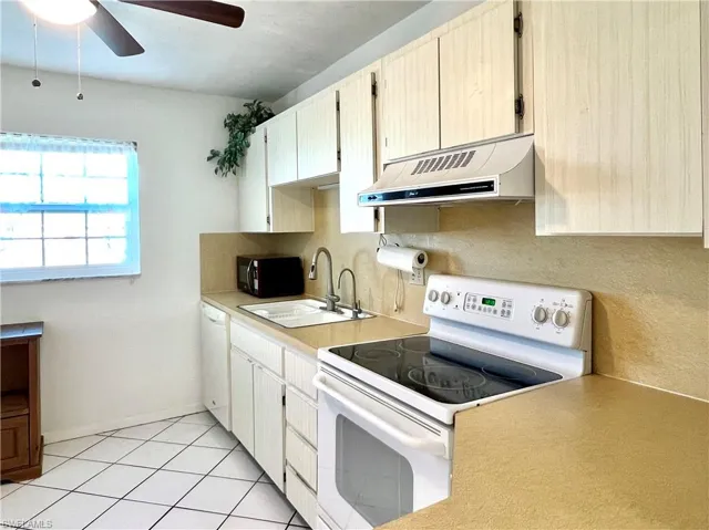 Kitchen with white appliances, exhaust hood, light tile patterned floors, light countertops, and ceiling fan
