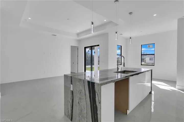 Kitchen with a large island, a tray ceiling, decorative light fixtures, and stone countertops