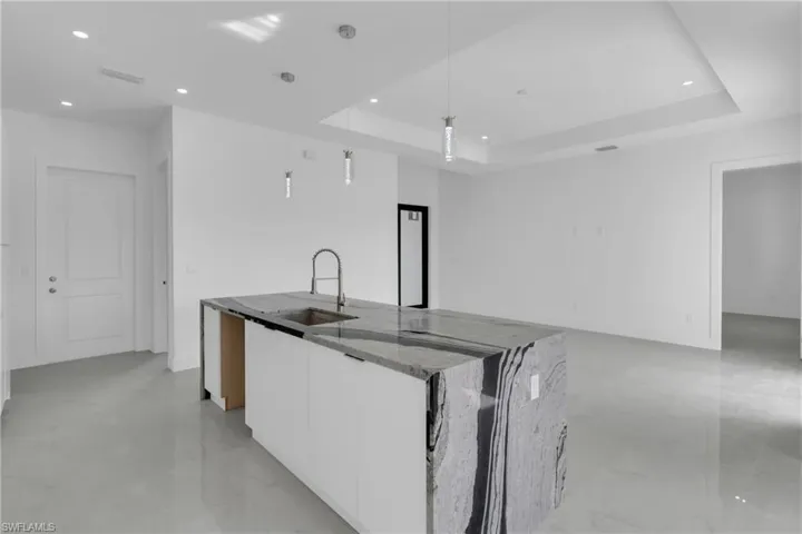 Kitchen with stone countertops, sink, decorative light fixtures, a tray ceiling, and white cabinets