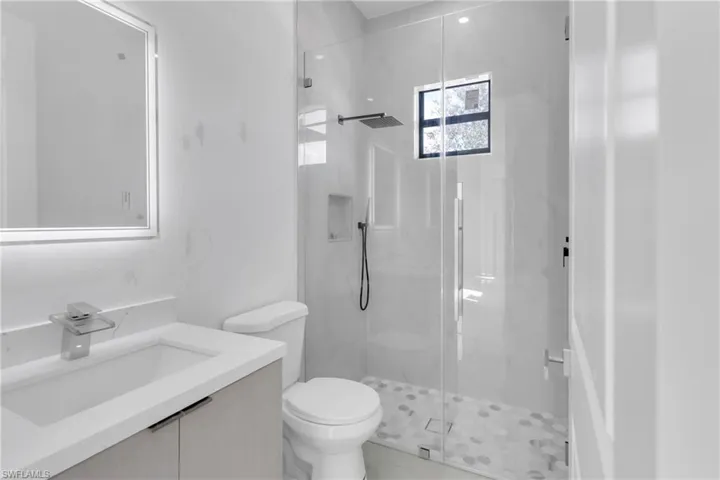 Bathroom featuring toilet, vanity, and a shower with door