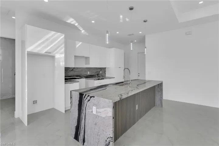 Kitchen featuring tasteful backsplash, light stone counters, pendant lighting, sink, and white cabinets