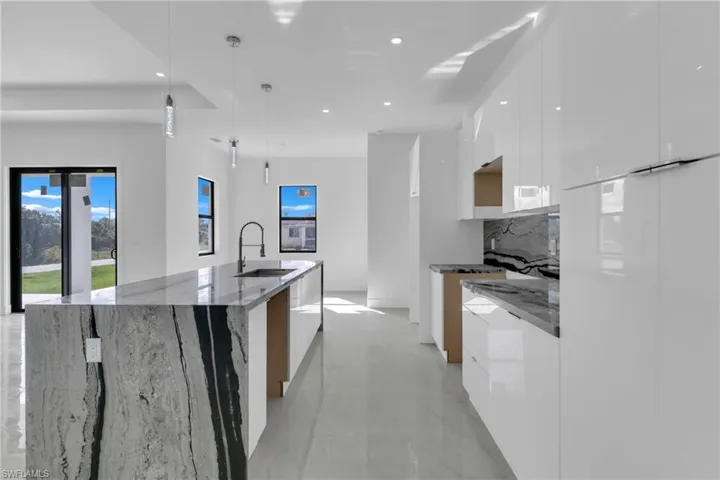 Kitchen featuring white cabinetry, backsplash, decorative light fixtures, stone counters, and a spacious island