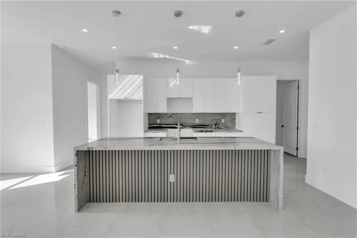 Kitchen featuring a center island with sink, white cabinets, decorative backsplash, light stone countertops, and pendant lighting