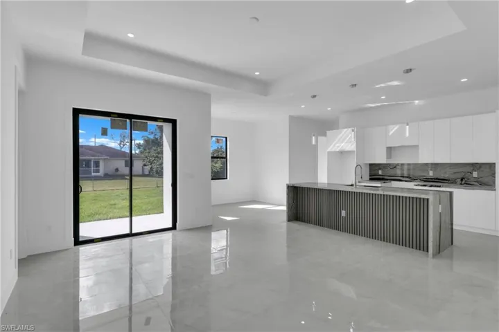 Kitchen with white cabinets, sink, a kitchen island with sink, backsplash, and a tray ceiling
