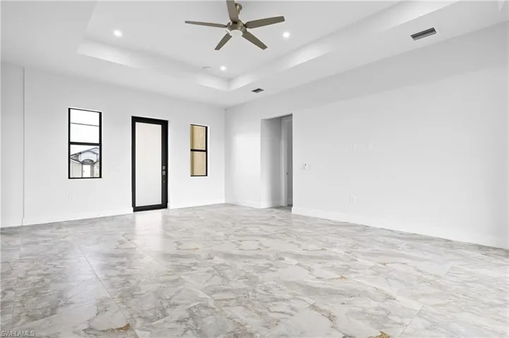Empty room featuring light marble finish floors, ceiling fan, a raised ceiling, and recessed lighting