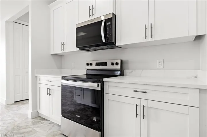 Kitchen featuring stainless steel appliances, light marble finish flooring, white cabinetry, and light stone countertops