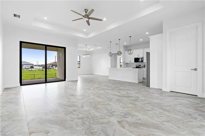 Unfurnished living room with a tray ceiling, light marble finish floors, ceiling fan, and recessed lighting