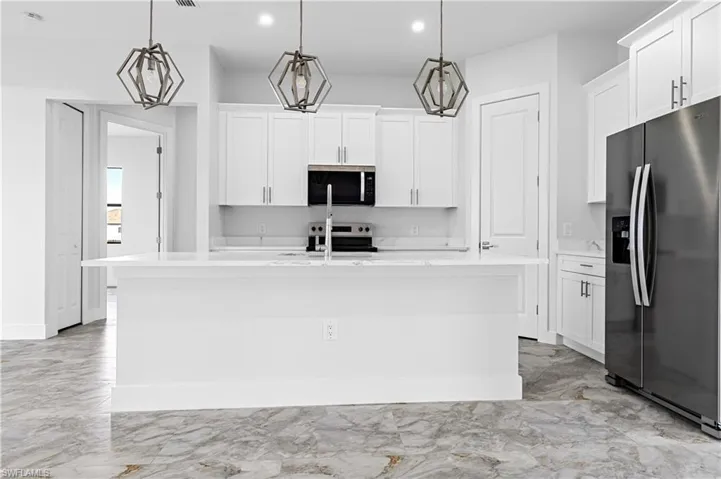 Kitchen featuring appliances with stainless steel finishes, light marble finish flooring, light countertops, white cabinetry, and recessed lighting