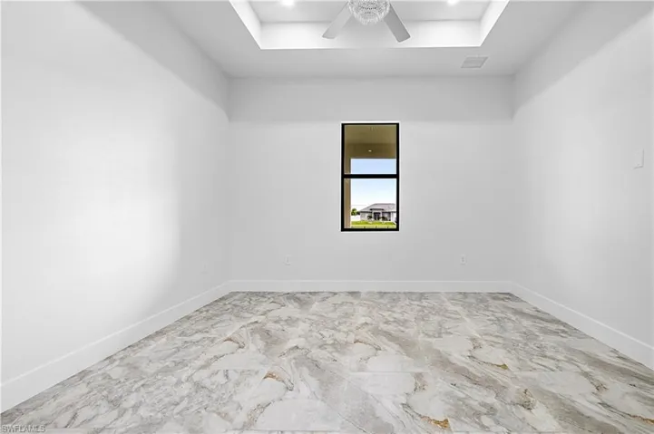 Unfurnished room featuring a tray ceiling, ceiling fan, and marble finish flooring
