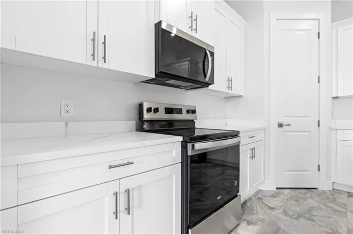 Kitchen with appliances with stainless steel finishes, light marble finish flooring, white cabinets, and light stone countertops