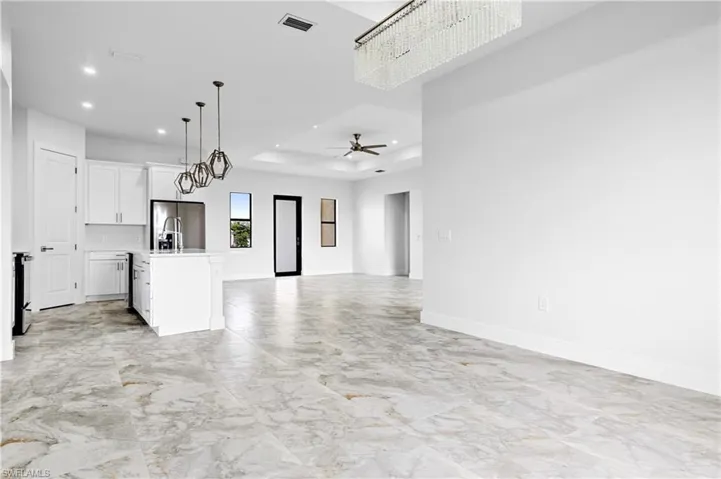 Unfurnished living room featuring recessed lighting, ceiling fan, a tray ceiling, and light marble finish floors