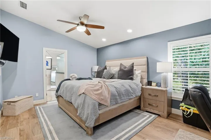 Bedroom with vaulted ceiling, light wood finished floors, a ceiling fan, recessed lighting, and ensuite bath