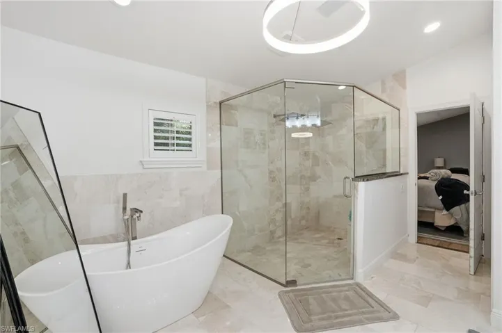 Full bath featuring ensuite bath, tile walls, a freestanding tub, a shower stall, and recessed lighting