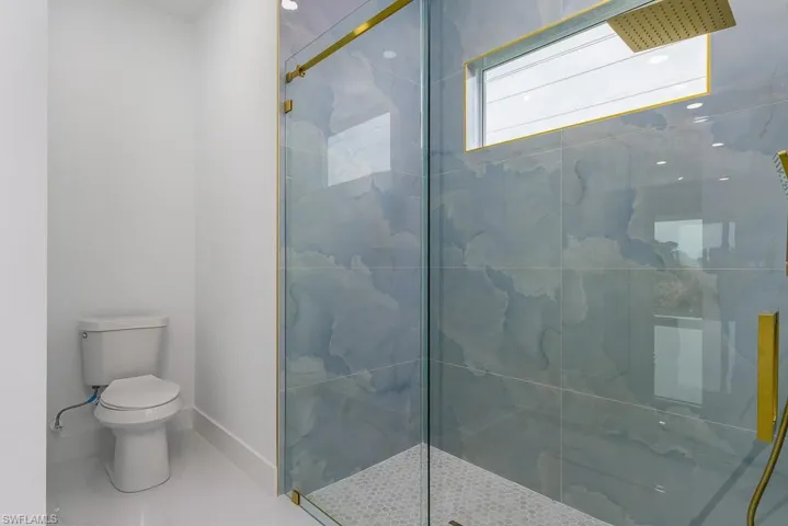 Bathroom featuring a shower with shower door, tile flooring, and toilet