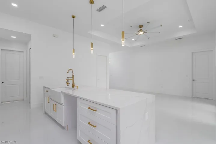 Kitchen featuring hanging light fixtures, ceiling fan, a tray ceiling, a kitchen island with sink, and sink