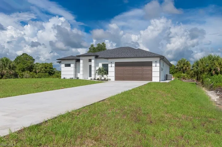 View of front of property with a garage, central air condition unit, and a front lawn