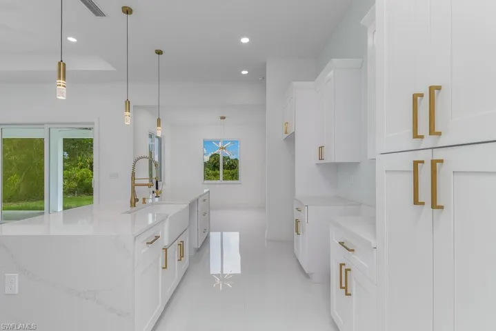 Kitchen featuring light stone countertops, an island with sink, pendant lighting, light tile floors, and white cabinetry