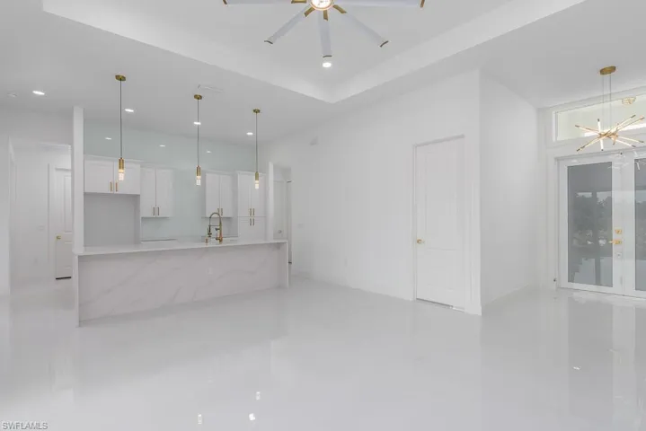 Unfurnished living room featuring a raised ceiling, ceiling fan with notable chandelier, sink, and light tile floors