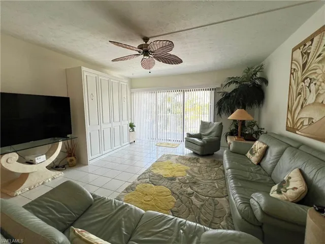 Living area featuring white tile flooring, a tropical-style ceiling fan, and Murphy bed