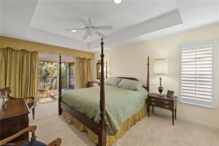 Carpeted bedroom with ceiling fan, a raised ceiling, and access to outside