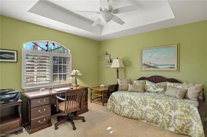 Bedroom featuring light colored carpet, a raised ceiling, and ceiling fan