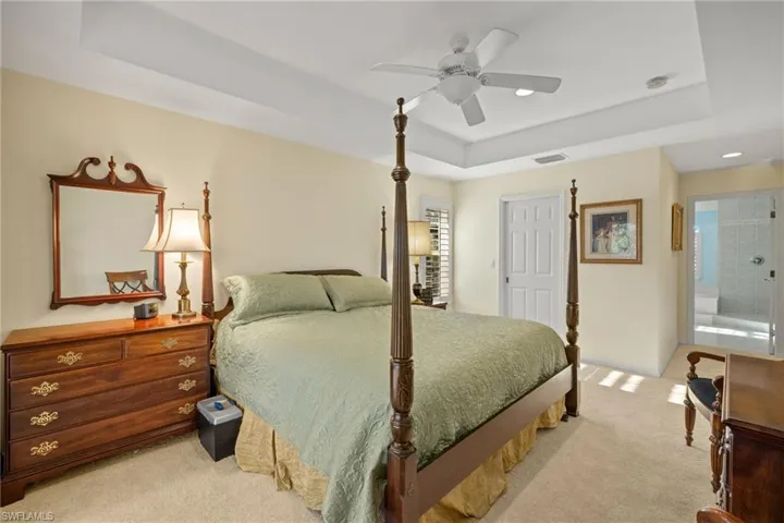 Bedroom featuring light carpet, ceiling fan, and a tray ceiling
