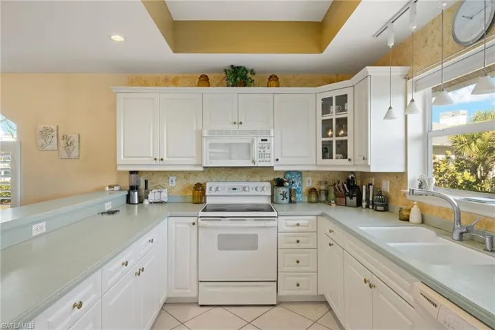 Kitchen with sink, white appliances, hanging light fixtures, and white cabinets