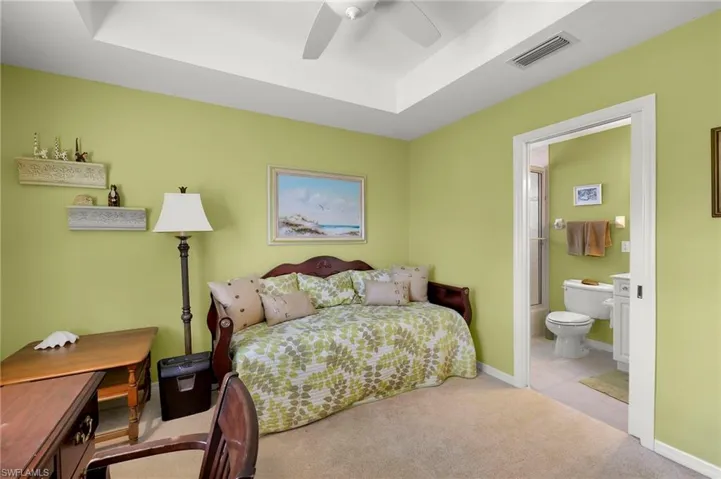 Carpeted bedroom with a tray ceiling, ceiling fan, and ensuite bathroom
