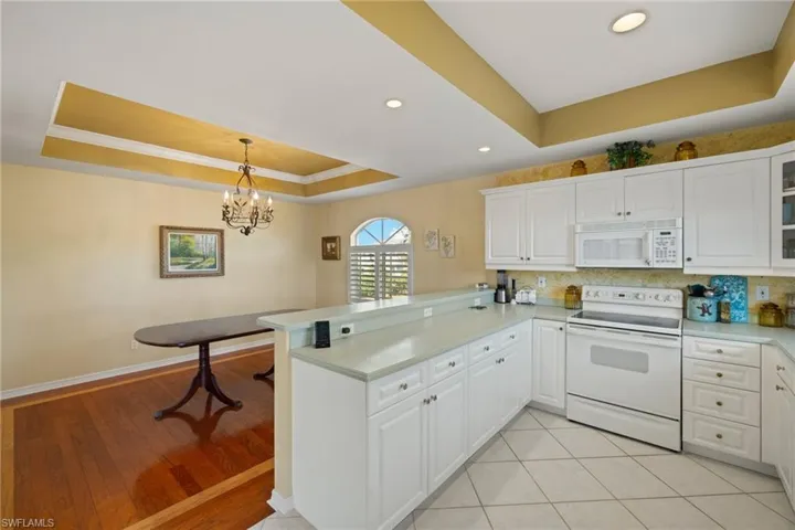 Kitchen featuring white cabinetry, a tray ceiling, white appliances, and kitchen peninsula