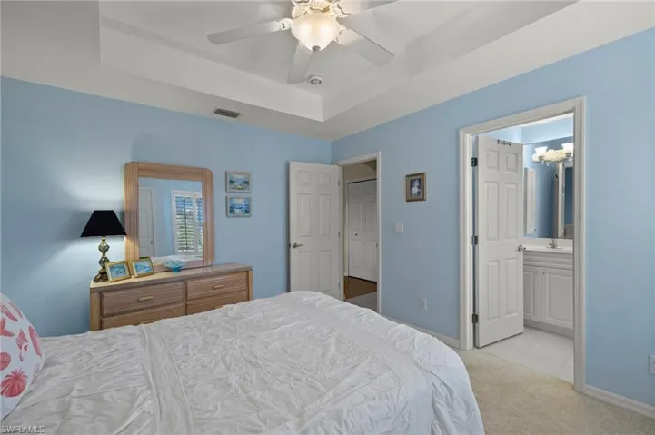 Carpeted bedroom featuring ceiling fan, a raised ceiling, and ensuite bath