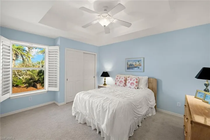 Carpeted bedroom with a closet, ceiling fan, and a tray ceiling