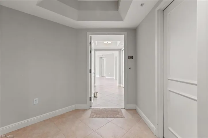 Corridor with a tray ceiling and light tile patterned floors