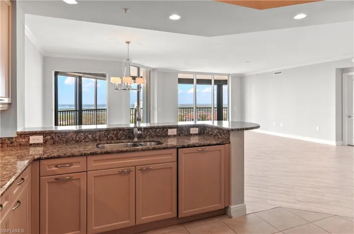 Kitchen with ornamental molding, dark stone countertops, open floor plan, plenty of natural light, and a peninsula