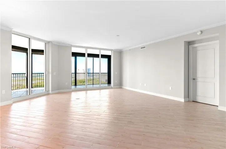 Empty room with crown molding, expansive windows, and light wood-style floors