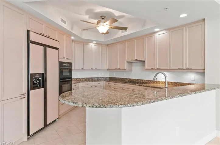 Kitchen featuring black appliances, a ceiling fan, cream cabinetry, a peninsula, and a tray ceiling