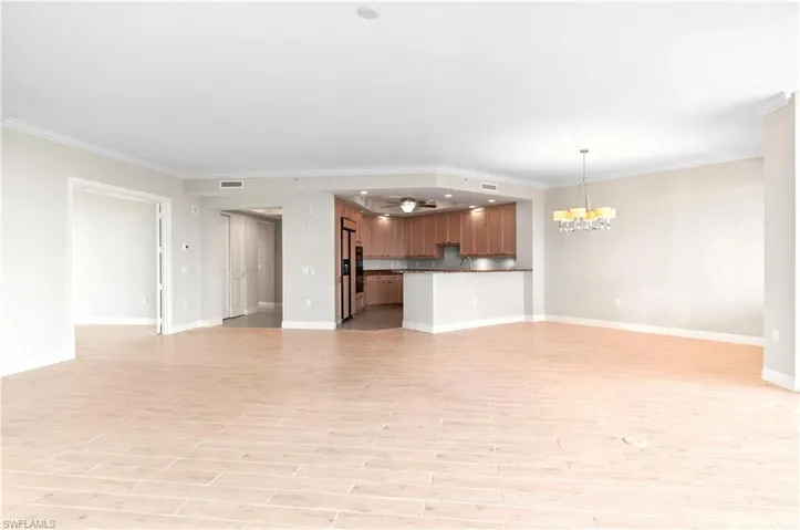 Unfurnished living room with hanging lights, ornamental molding, and light wood finished floors