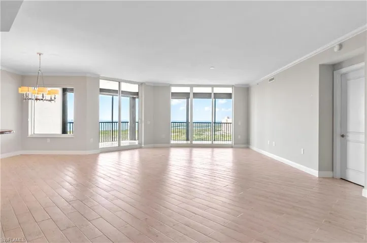 Unfurnished room featuring crown molding, expansive windows, hanging lights, and light wood-style flooring