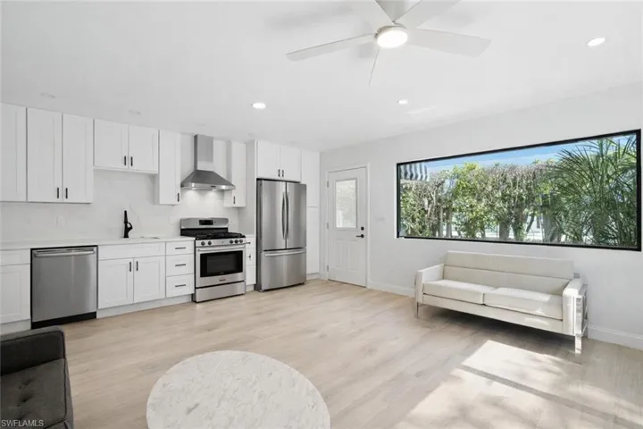 Kitchen with white cabinets, stainless steel appliances, wall chimney exhaust hood, light wood-type flooring, and recessed lighting