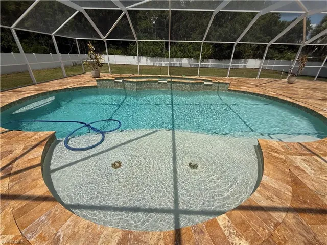 Screened pool enclosure featuring a curved swimming pool, integrated spa, and textured deck