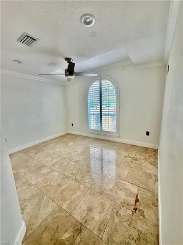 Spacious 2nd bedroom featuring polished tile flooring, an arched window with plantation shutters, crown molding, and a ceiling fan with integrated lighting
