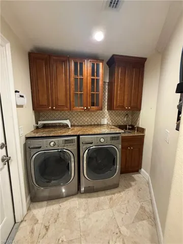 Utility room featuring wood cabinetry, granite-finish countertops, and a full-height tile backsplash