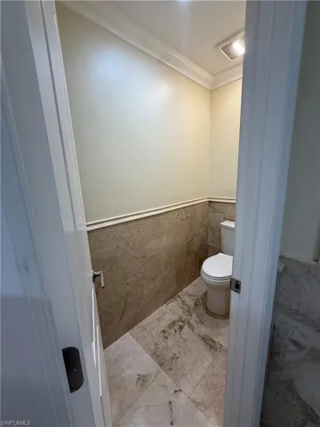 Master bathroom Powder room featuring crown molding, half-wall tile surround, and coordinating large format tile flooring