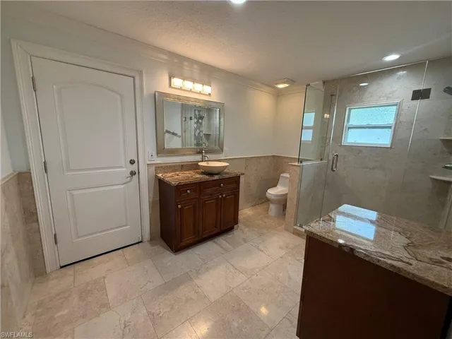 3rd Spacious bathroom featuring large format tile flooring and wainscoting, a walk-in shower with clear glass enclosure, a vanity with a vessel sink and granite countertop, and recessed lighting
