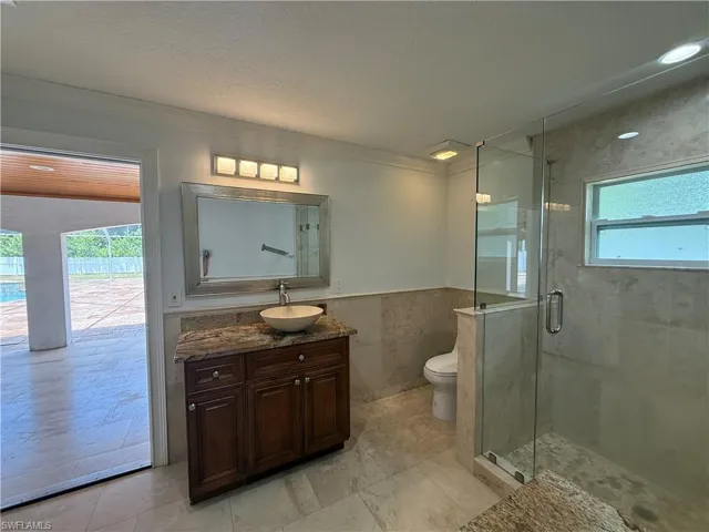 3rd Bathroom featuring a glass-enclosed shower, stone-finish tile flooring, a dark wood vanity with a vessel sink, a granite countertop, and a wall-mounted mirror