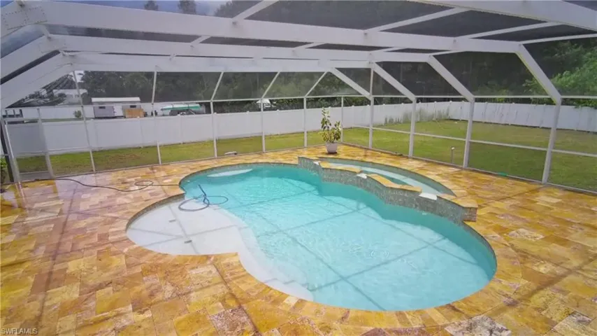 Screened lanai featuring a freeform pool with integrated spa and irregular flagstone decking