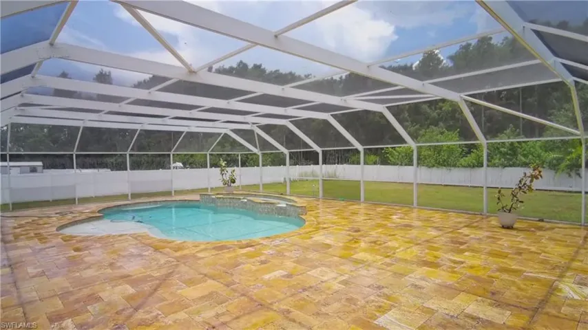 Screened pool enclosure featuring a freeform swimming pool, integrated spa, extensive paver decking, and a white privacy fence