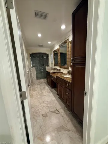 Spacious master bathroom featuring large format tile flooring, a dual vanity with integrated sinks and a stone countertop, dark wood cabinetry, and a glass-enclosed shower with tile surround