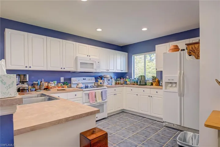 Kitchen featuring white appliances, white cabinets, light countertops, and a sink