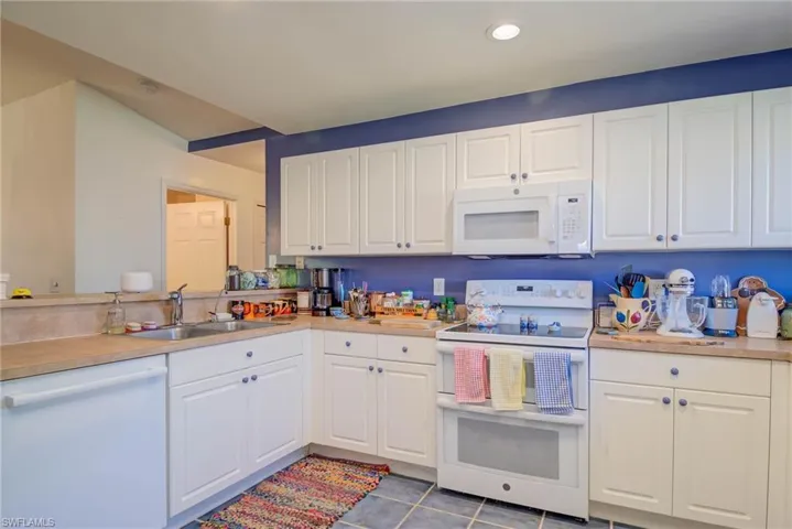 Kitchen with white appliances, white cabinetry, and a sink